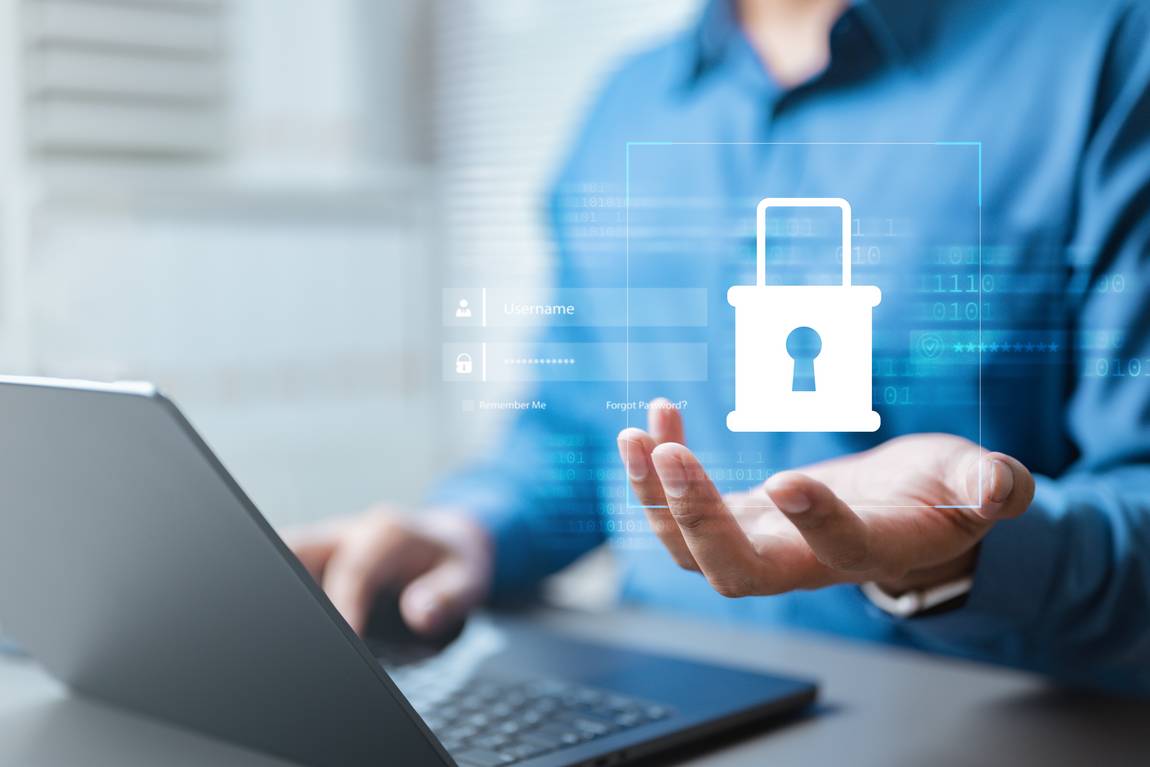 ©istock.com/Nutthaseth Vanchaichana Eine Person in einem blauen Hemd arbeitet an einem Laptop und hält ein digitales Symbol eines Vorhängeschlosses, das Online-Sicherheit und Datenschutz symbolisiert, mit schwebenden Login-Grafiken im Vordergrund.