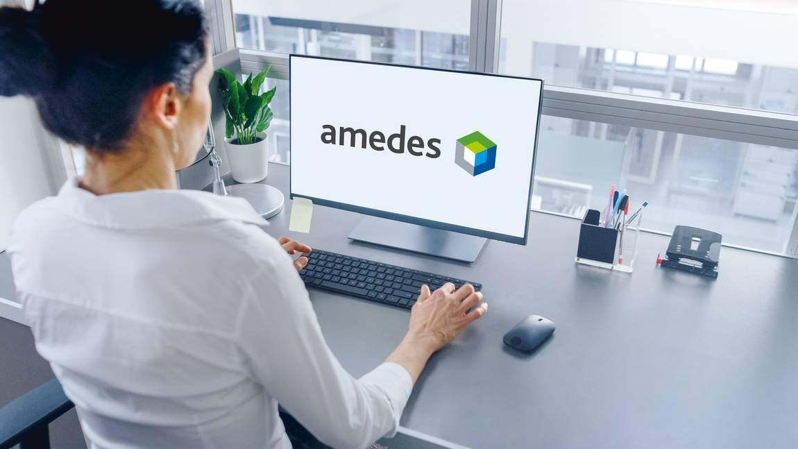 ©stock.adobe.com/Gorodenkoff Eine Frau sitzt an einem Schreibtisch und arbeitet an einem Computer, auf dem das amedes-Logo abgebildet ist, wobei ein Bürofenster, eine Pflanze, eine Tastatur, eine Maus und einige Schreibtischgegenstände zu sehen sind.